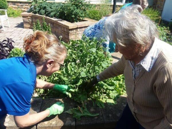 Resident in Memory Care gardens with the help of a caregiver