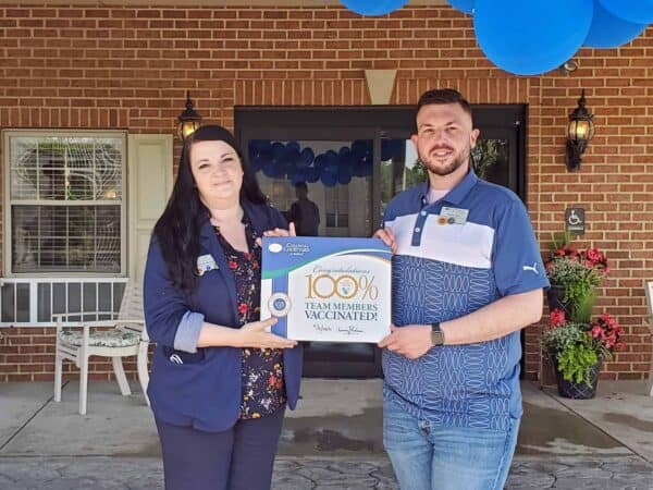 Photo Cutline information: IntegraCare Director of Operations Western Region Belinda McQuaide presents a certificate to Colonial Courtyard at Bedford Executive Operations Officer Brian Hall. Colonial Courtyard at Bedford attained 100% COVID-19 vaccinations among team members.