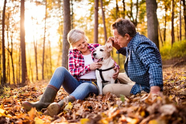 Senior couple outside in fall weather surrounded by leaves with their dog