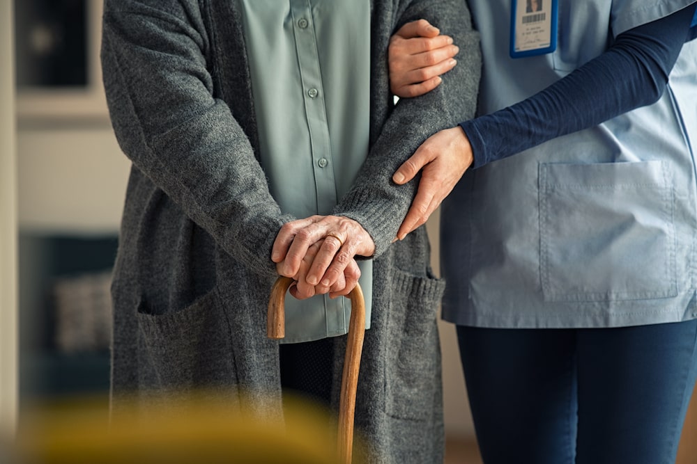 A senior walking with a cane and a nurse