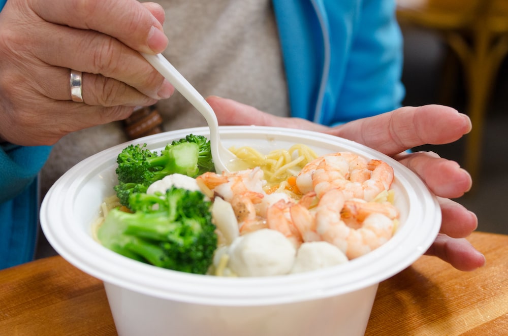 A senior eating a bowl of shrimp ramen with veggies