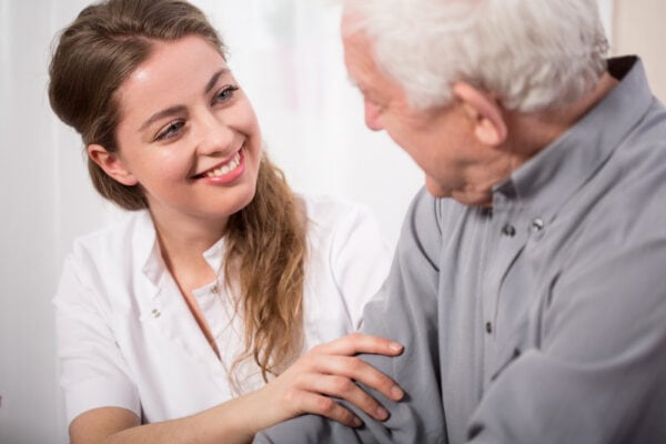 A senior man and a happy nurse sit together and chat