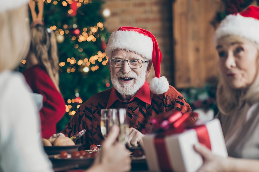 A senior man wearing a Santa hat while smiling and laughing