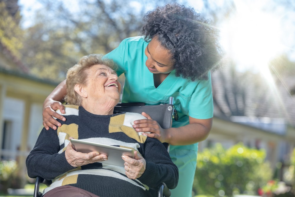 A senior resident and a caregiver smile at one another