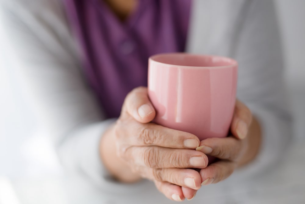 A senior woman holds onto a hot cup of coffee