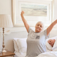 A happy senior woman stretching and yawning as she wakes up