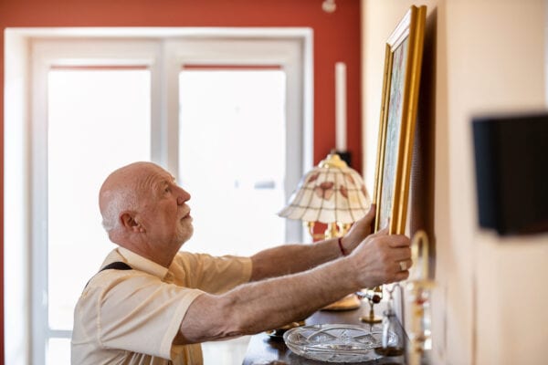 A senior man hanging up a painting in his apartment