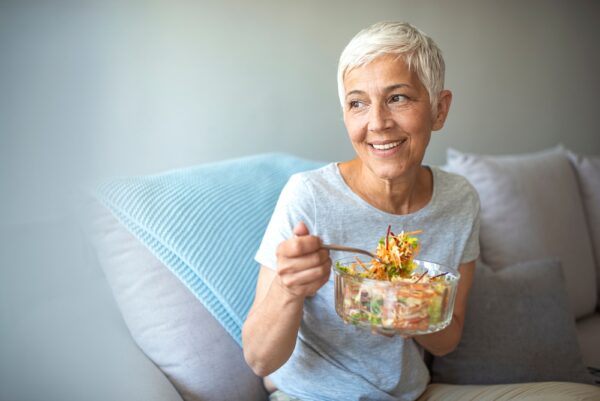 A smiling senior woman eating a bowl of healthy salad