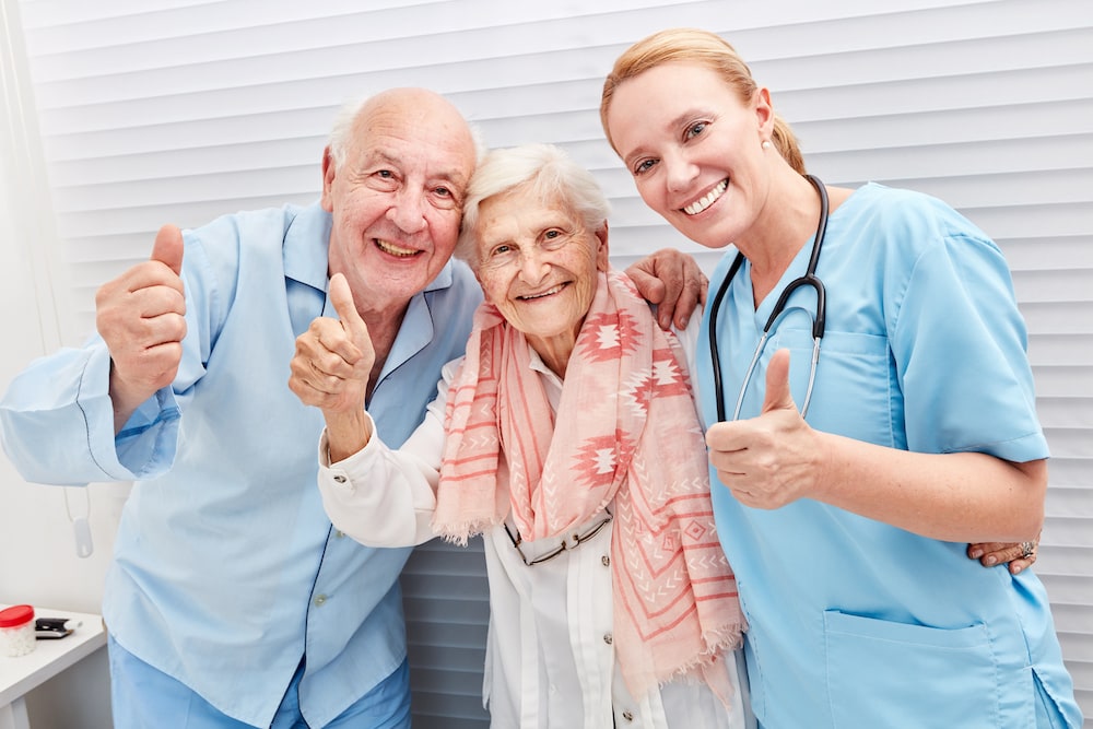 A senior couple and a nurse give a thumbs up