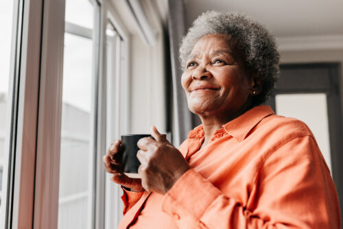 Senior woman holding mug, smiling and looking into distance beside