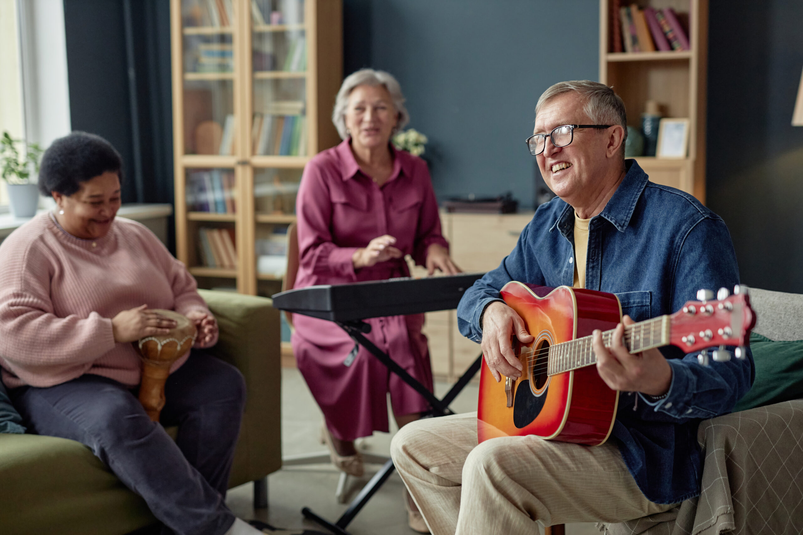 Group of joyful senior people playing music together enjoying talent show in retirement home focus on smiling senior man playing guitar copy space