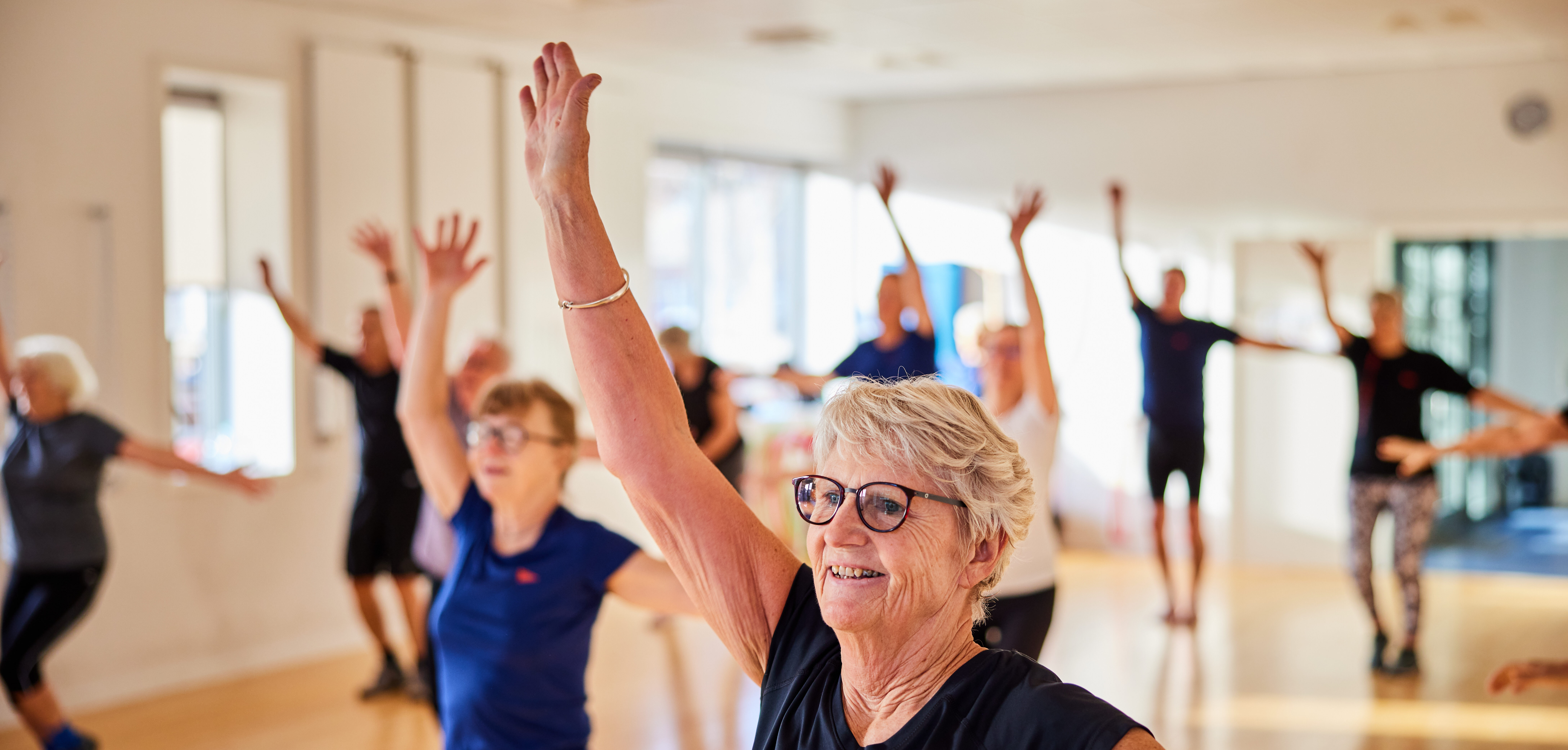 Smiling senior woman in sportswear doing an aerobics exercise class with other seniors in a health club