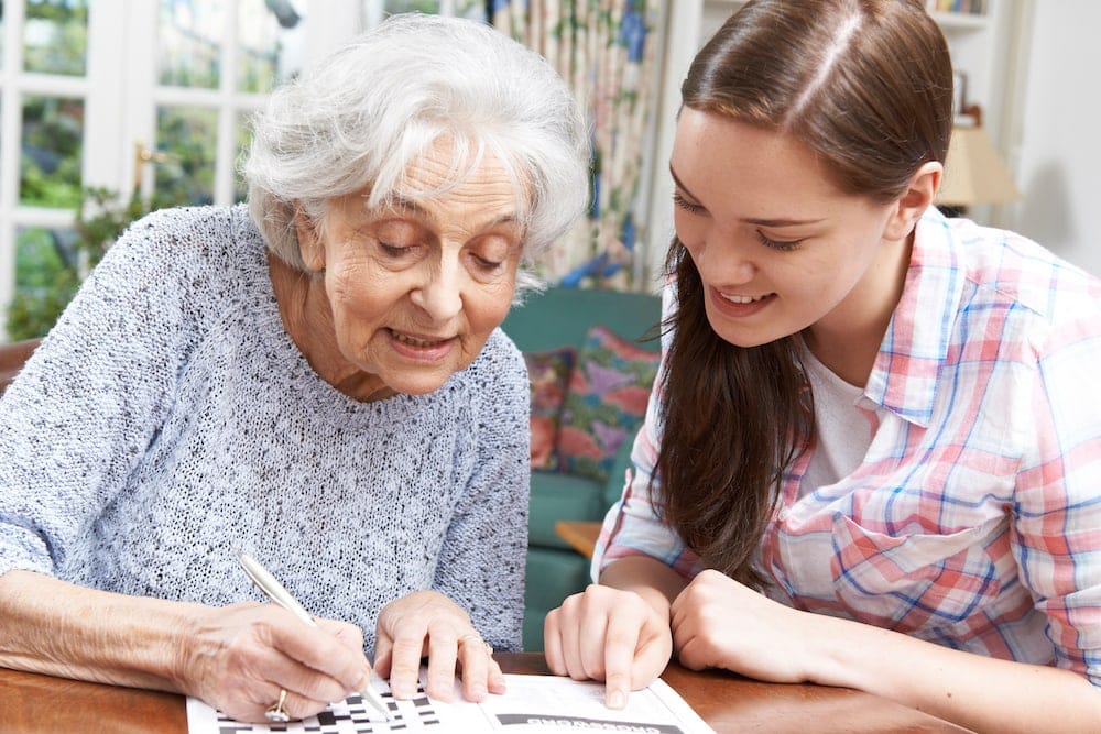 Resident and staff of an assisted living community enjoying a crossword puzzle during summer.