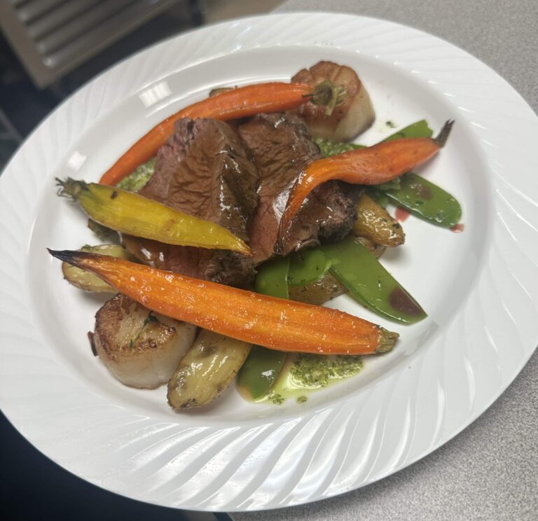 Beef with roasted carrots, scallops, fingerling potatoes, and snap peas on a white plate